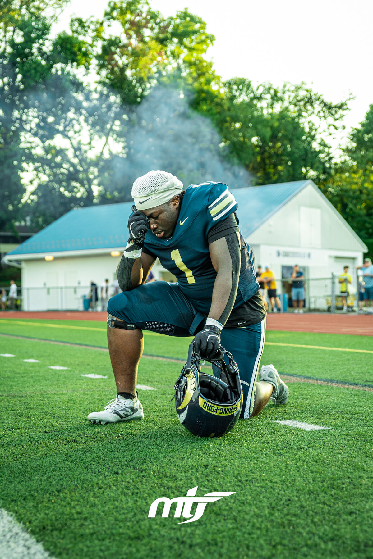 Football player kneeling on the sideline catching his breath, helmet resting on the turf